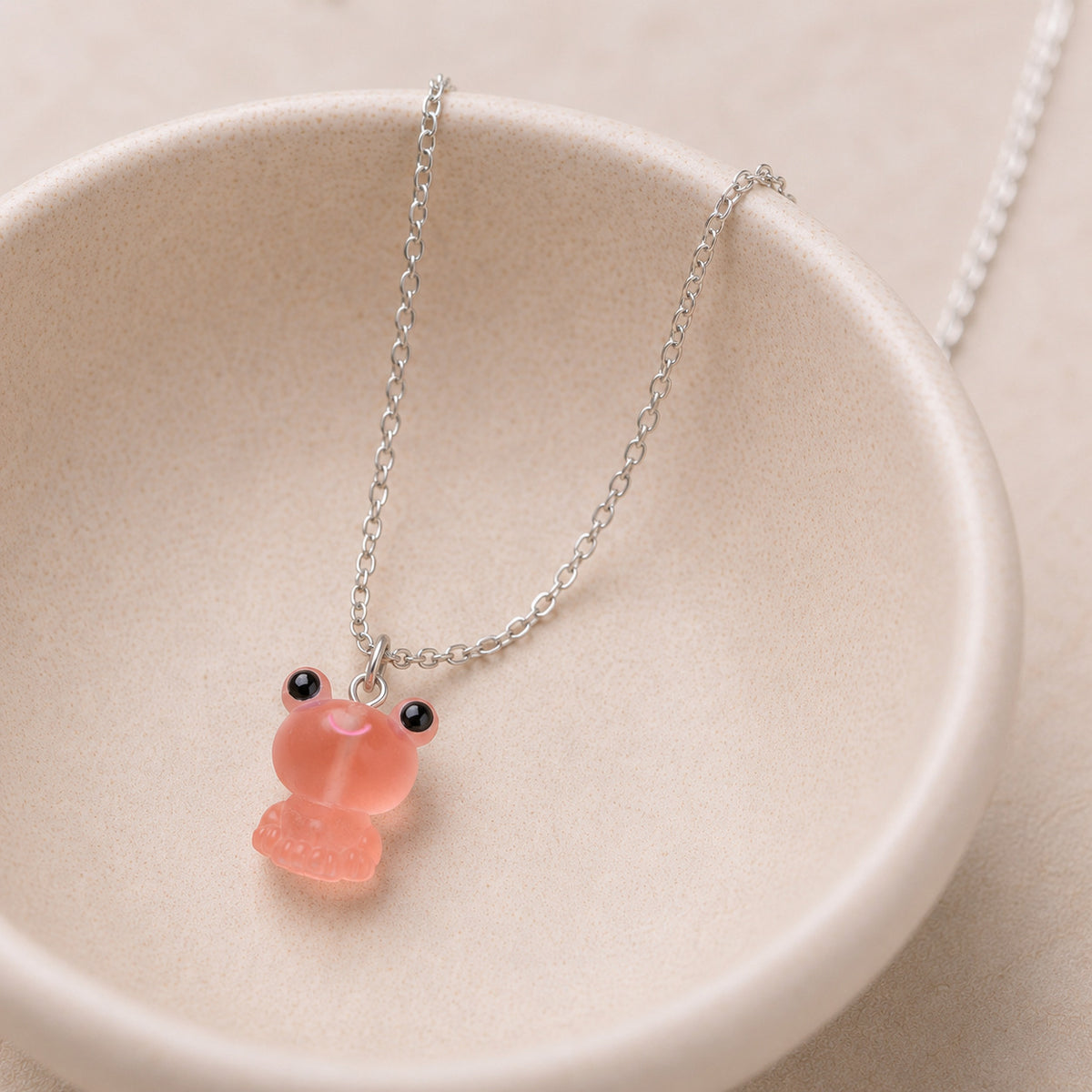Frosted Frog in Coral Necklace displayed on a ceramic bowl