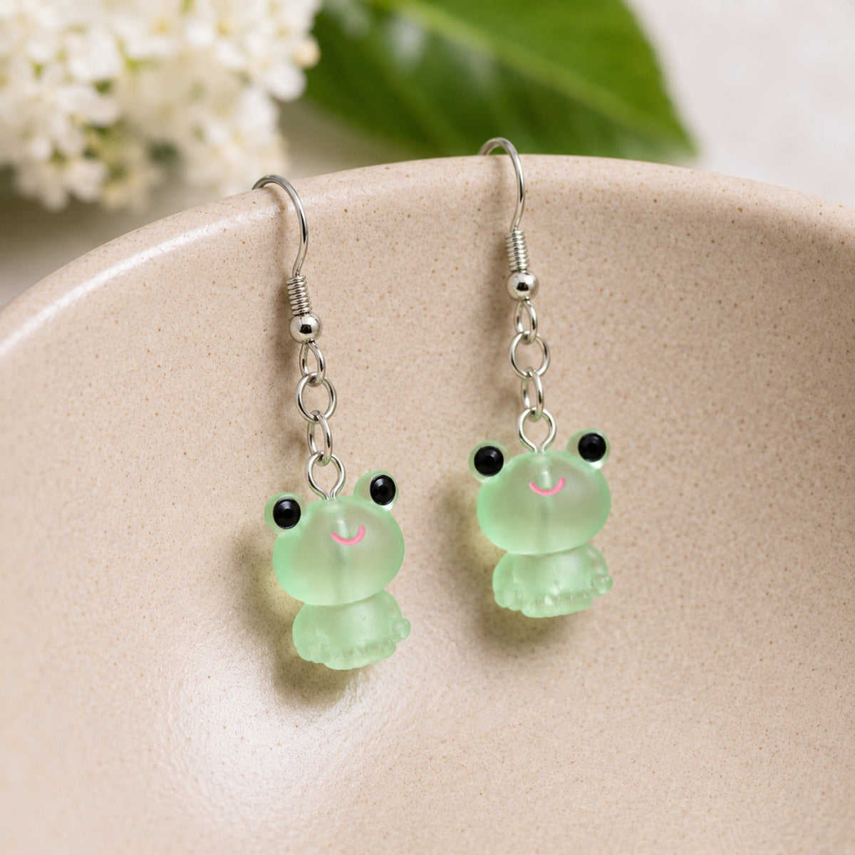 Frosted Frog in Green Earrings hooked over a ceramic bowl