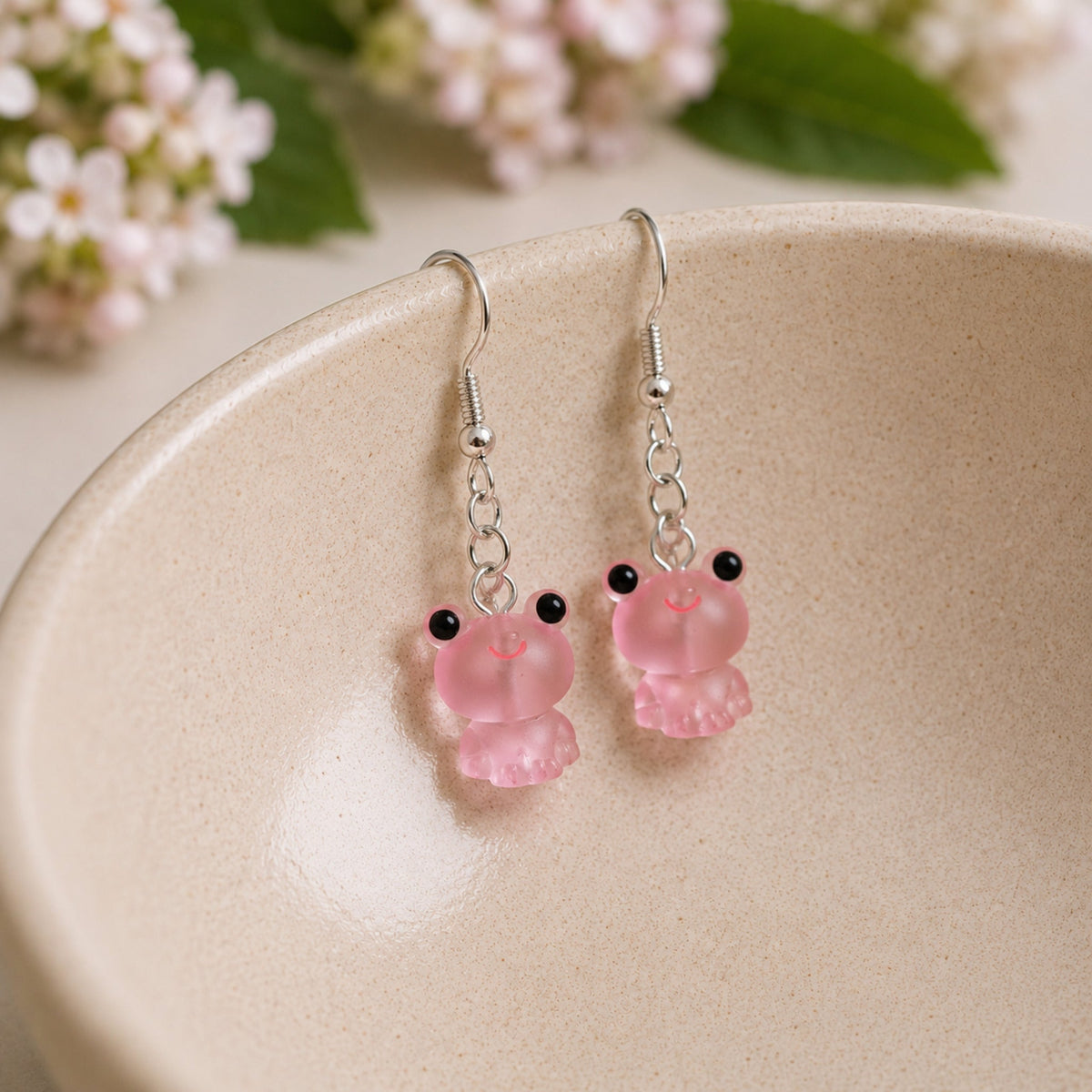 Frosted Frog in Pink Earrings hooked over a ceramic bowl