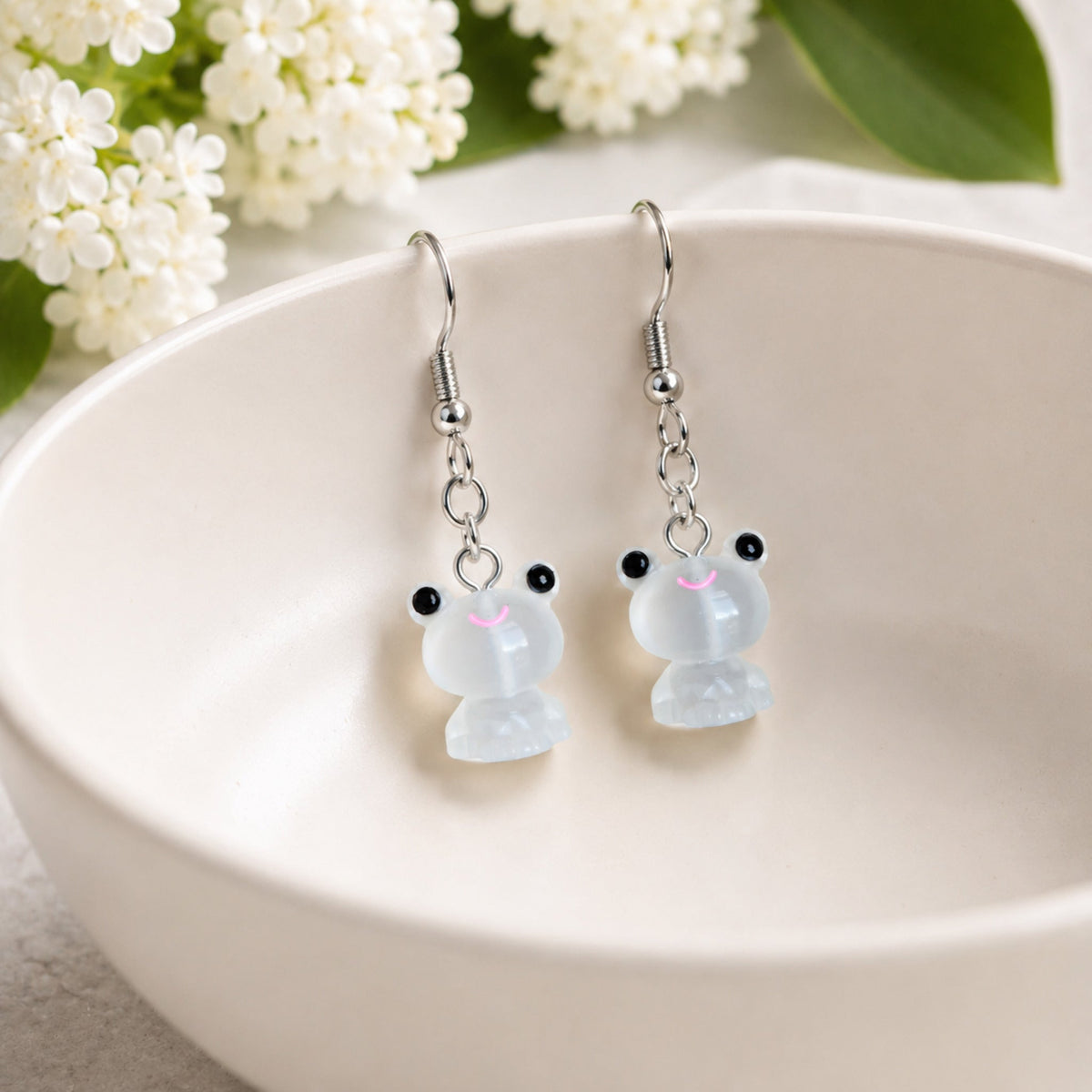 Frosted Frog in White Earrings displayed on a ceramic bowl