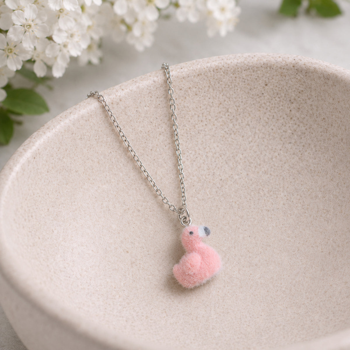 Fuzzy Flamingo Necklace hanging over a ceramic bowl