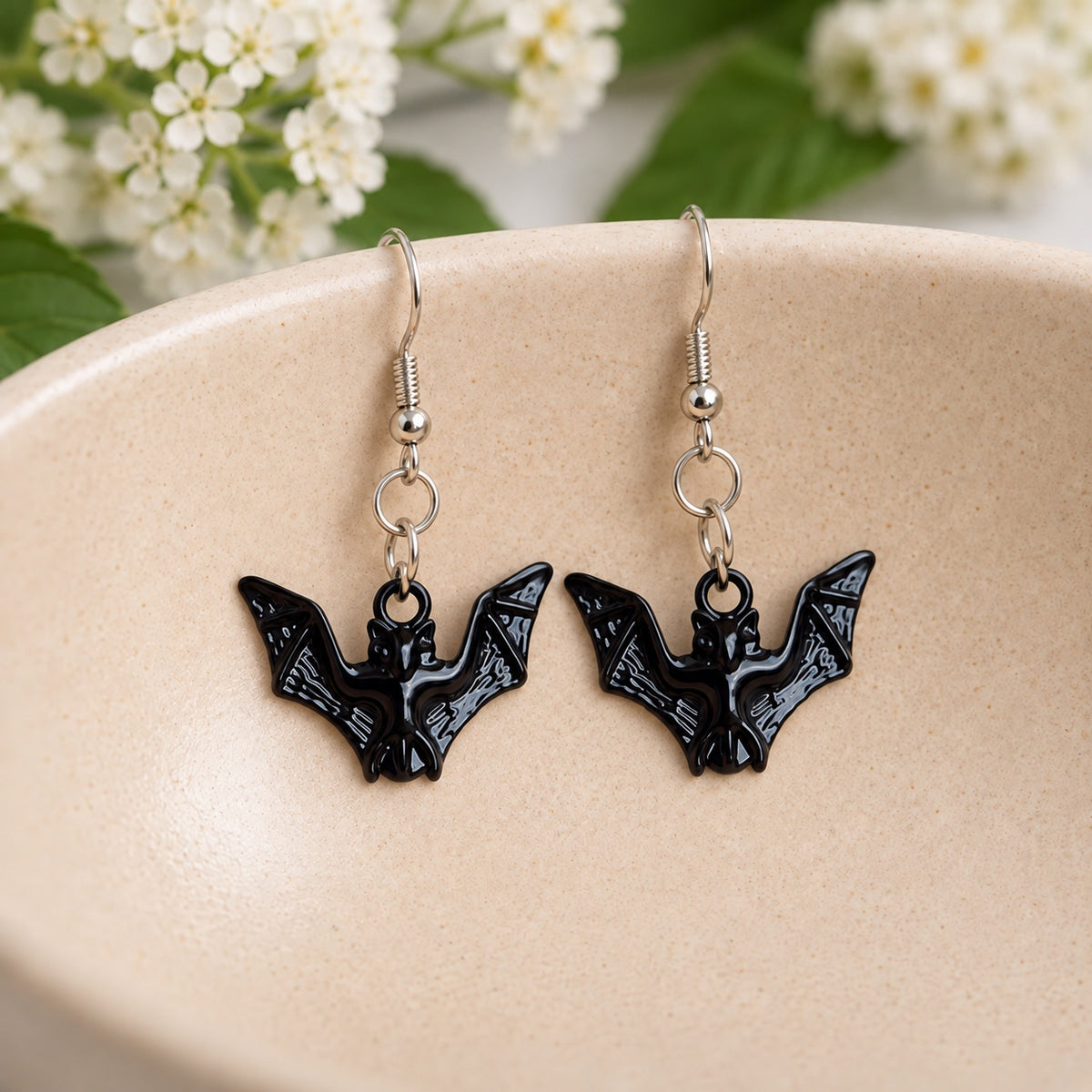 Pair of glossy black bat earrings in a cream speckled ceramic bowl