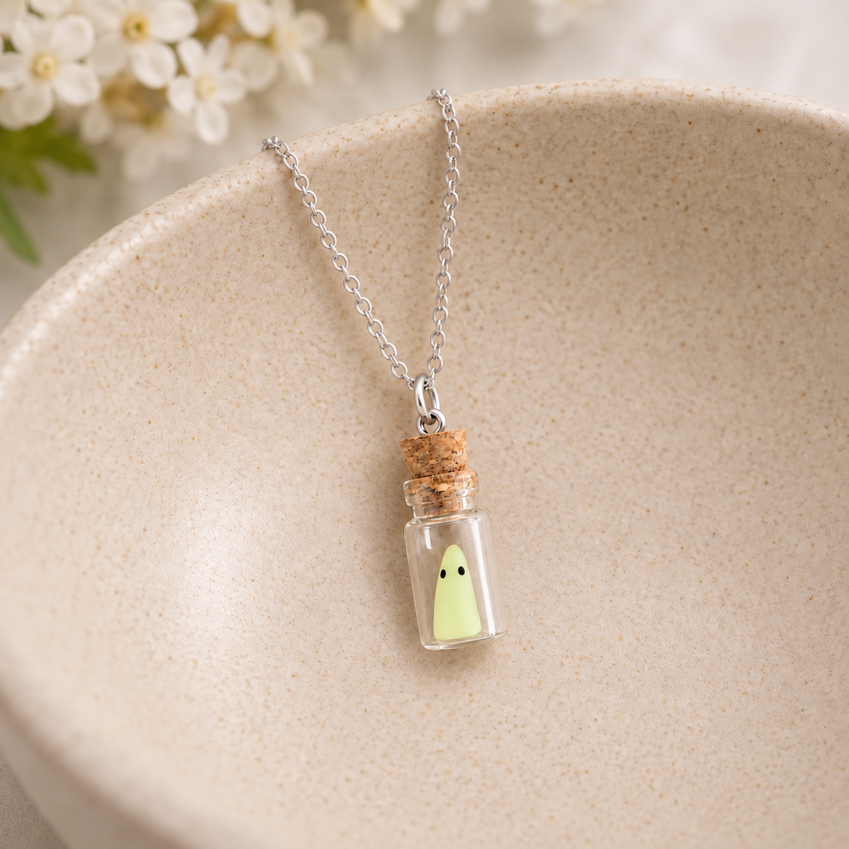 Ghost in a glass bottle necklace with silver-tone chain resting in a speckled ceramic bowl