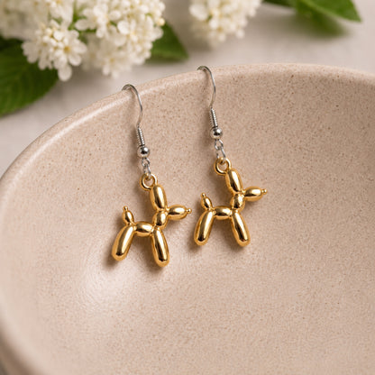Gold Balloon Dog Earrings hanging from a ceramic bowl