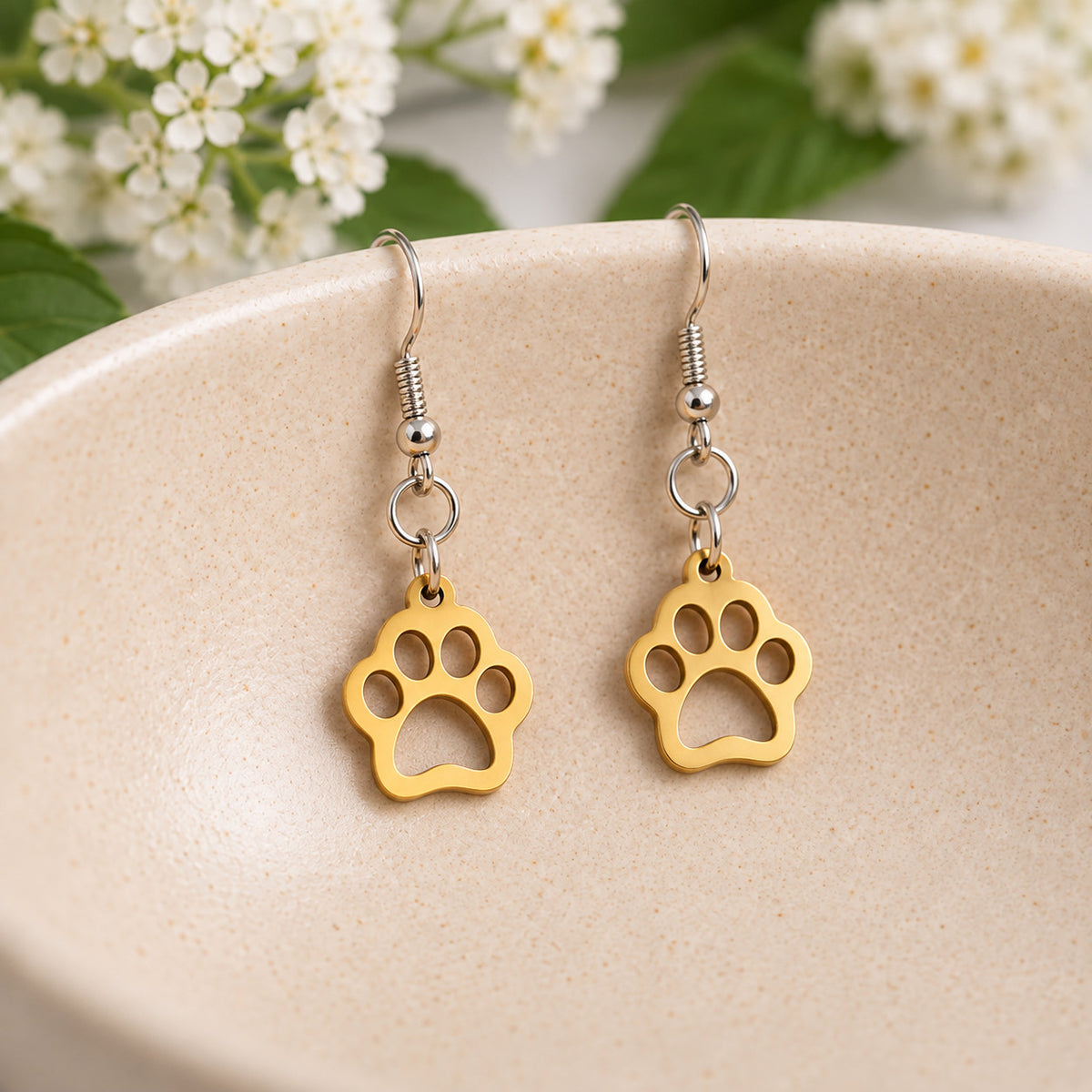 Gold paw print earrings resting in a speckled ceramic bowl