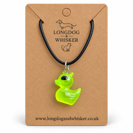 Green alien duck necklace on a black cord, displayed on its Longdog & Whisker kraft card