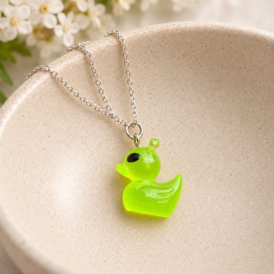 Translucent green alien duck necklace with silver-tone chain in a ceramic jewellery bowl