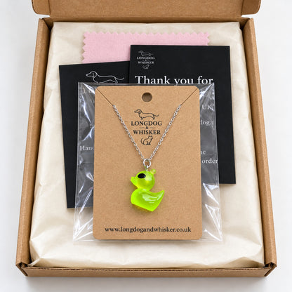 Green alien duck necklace on its product card in gift-ready packaging