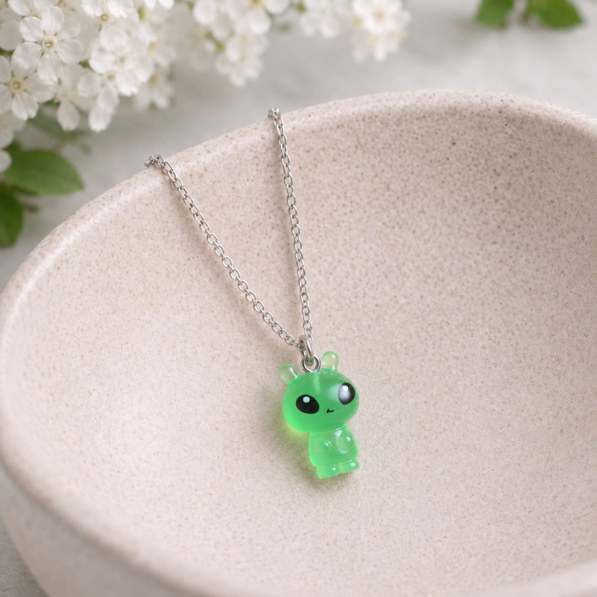 Little Green Alien Necklace hanging over a ceramic bowl