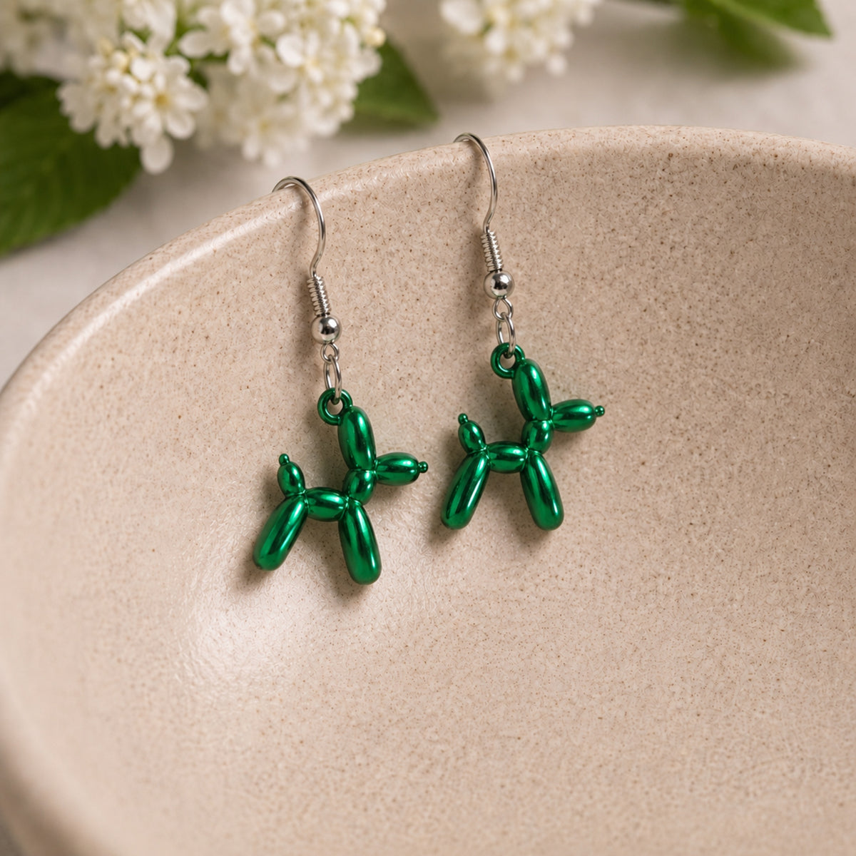 Green Balloon Dog Earrings hanging from a ceramic bowl