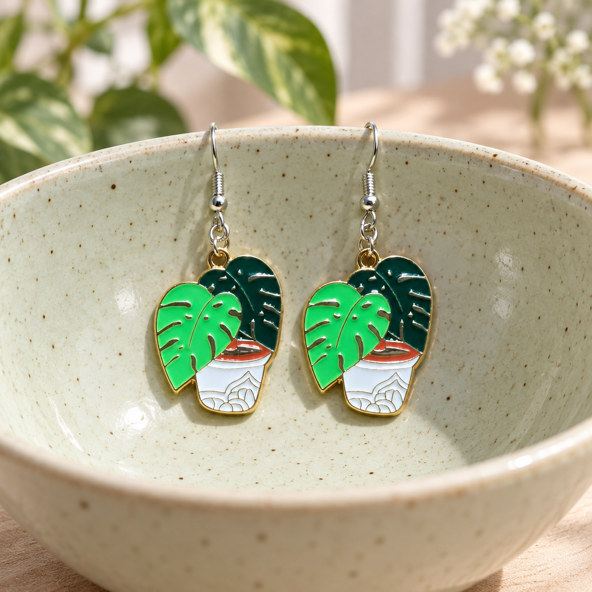 Green Monstera Earrings hanging from a ceramic bowl with silver hooks