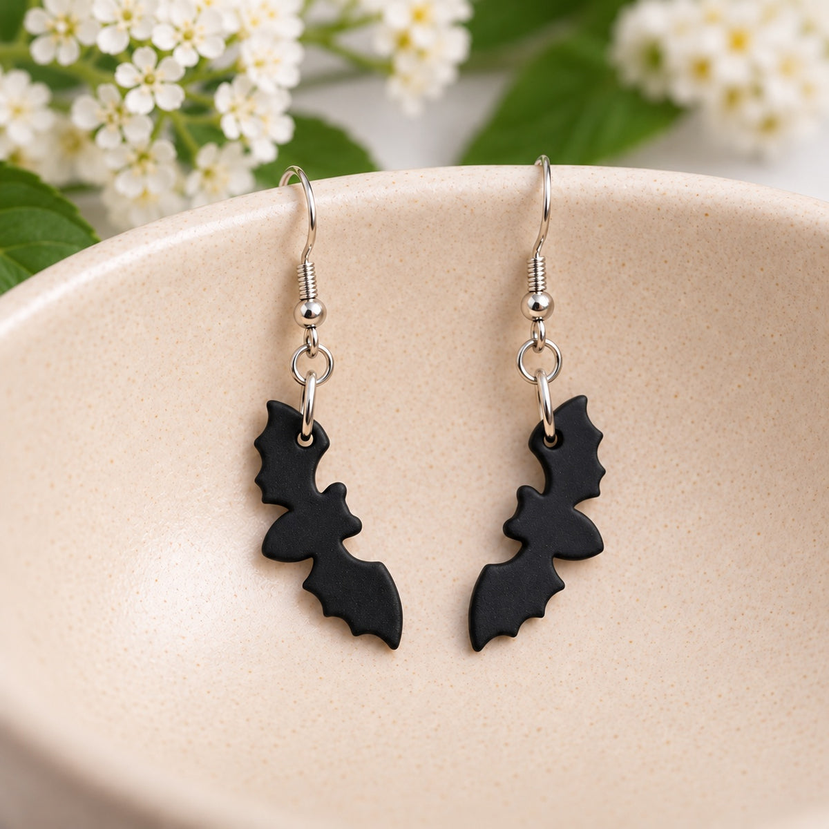 Pair of matte black bat earrings resting in a cream speckled ceramic bowl
