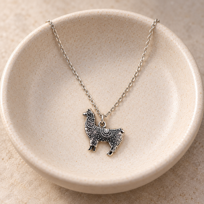 Ornate silver-tone llama pendant necklace in a ceramic bowl