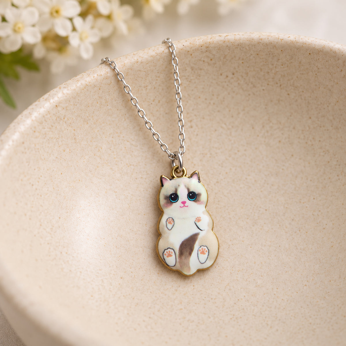 Ragdoll belly-up cat pendant necklace resting in a speckled ceramic bowl