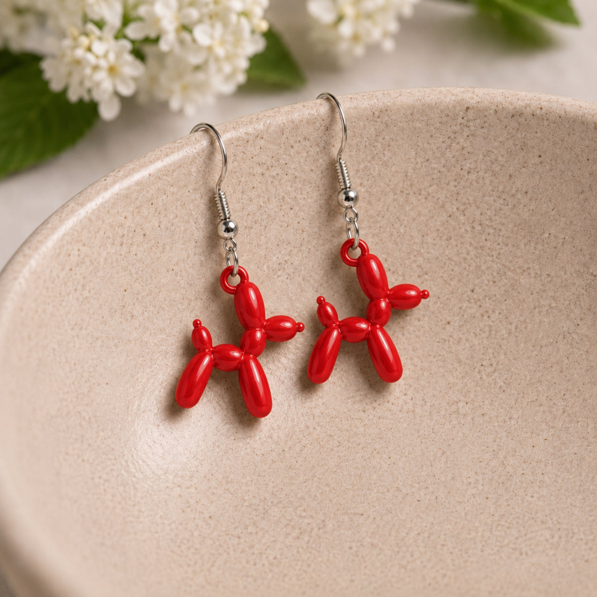 Red Balloon Dog Earrings hanging from a ceramic bowl