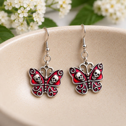 Pair of red skull butterfly earrings displayed in a cream ceramic bowl