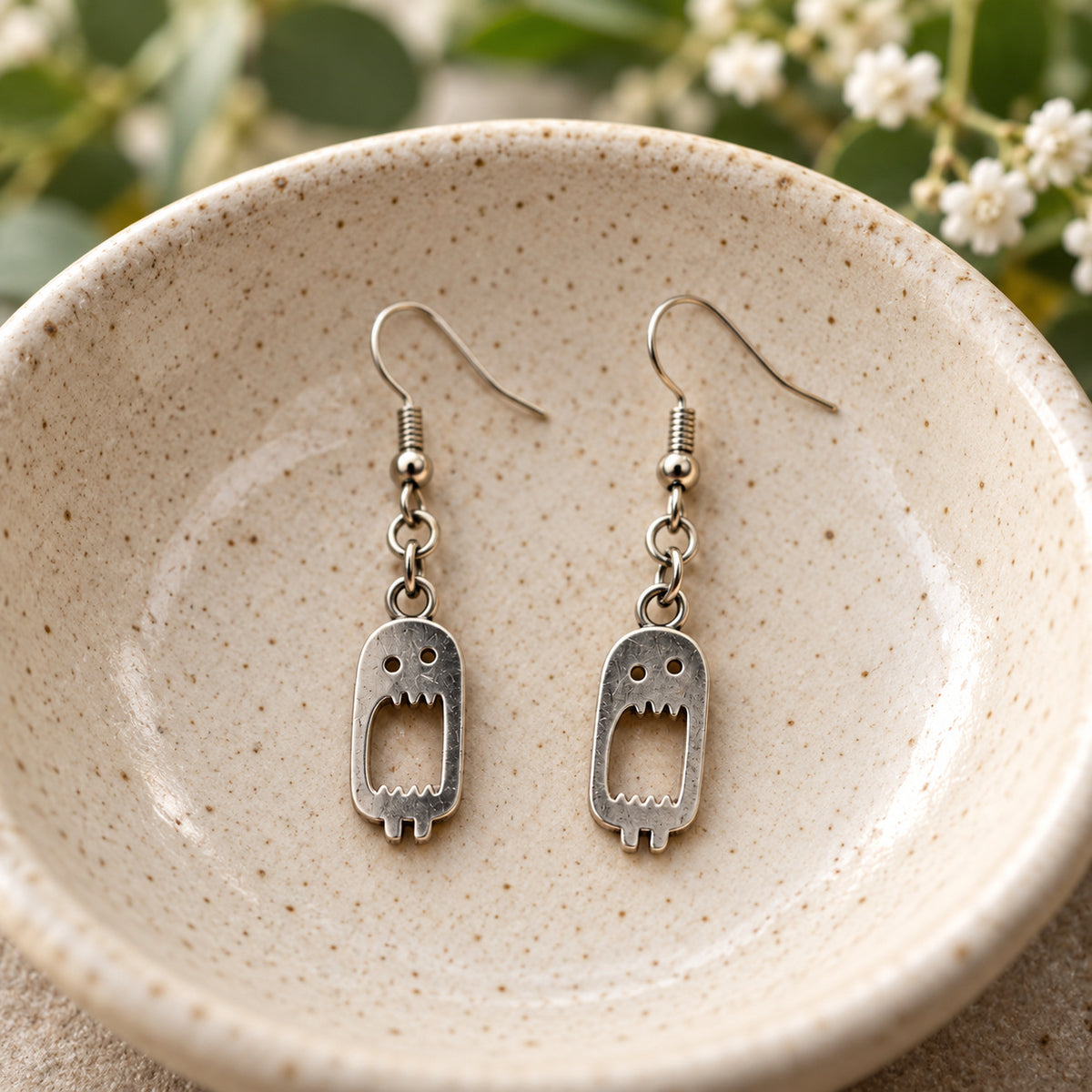Screaming monster drop earrings in a speckled ceramic bowl