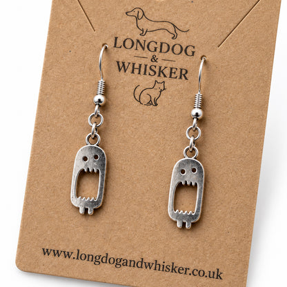 Close-up of silver screaming monster drop earrings on kraft card