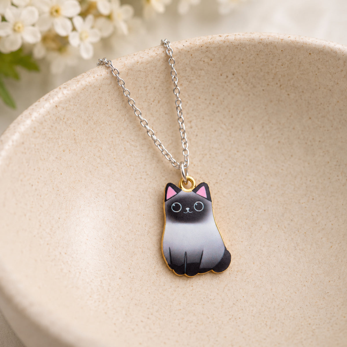 Siamese cat pendant necklace resting in a speckled ceramic bowl