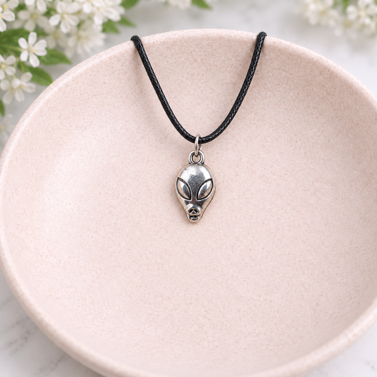 Silver Alien Head Necklace displayed in a pale pink bowl