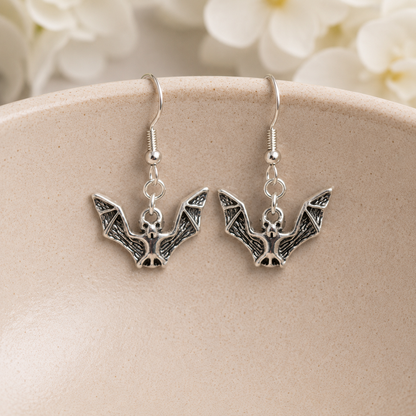 Silver Bat Drop Earrings hanging on a ceramic bowl