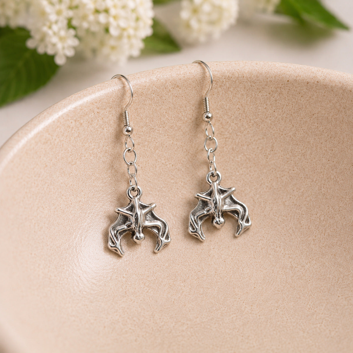 Silver bat earrings hanging inside a ceramic bowl