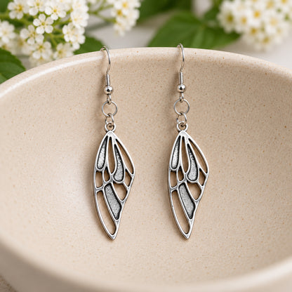 Silver-tone butterfly wing earrings hanging in a speckled ceramic bowl