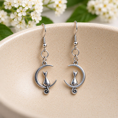 Silver cat and moon earrings resting in a speckled ceramic bowl.