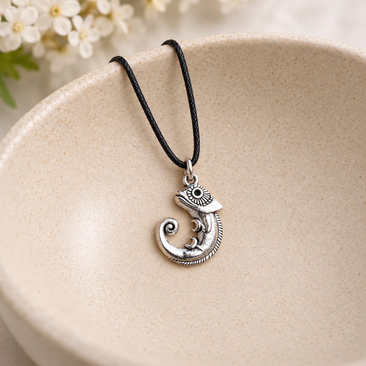 Silver-tone chameleon pendant on black cord resting in a speckled ceramic bowl