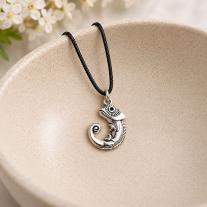 Silver-tone chameleon pendant on black cord resting in a speckled ceramic bowl