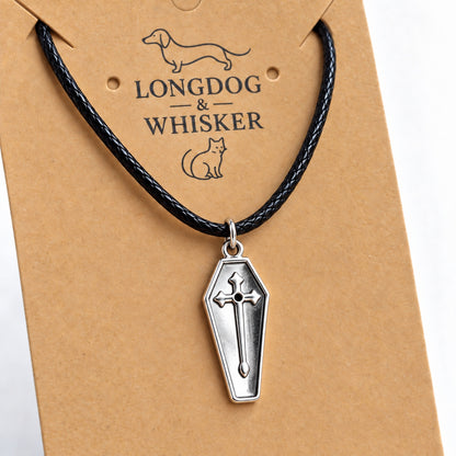 Close-up of the silver coffin pendant with raised cross, polished rim and black cord.