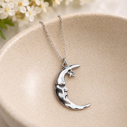 Silver-tone moon face and star pendant necklace resting in a speckled ceramic bowl