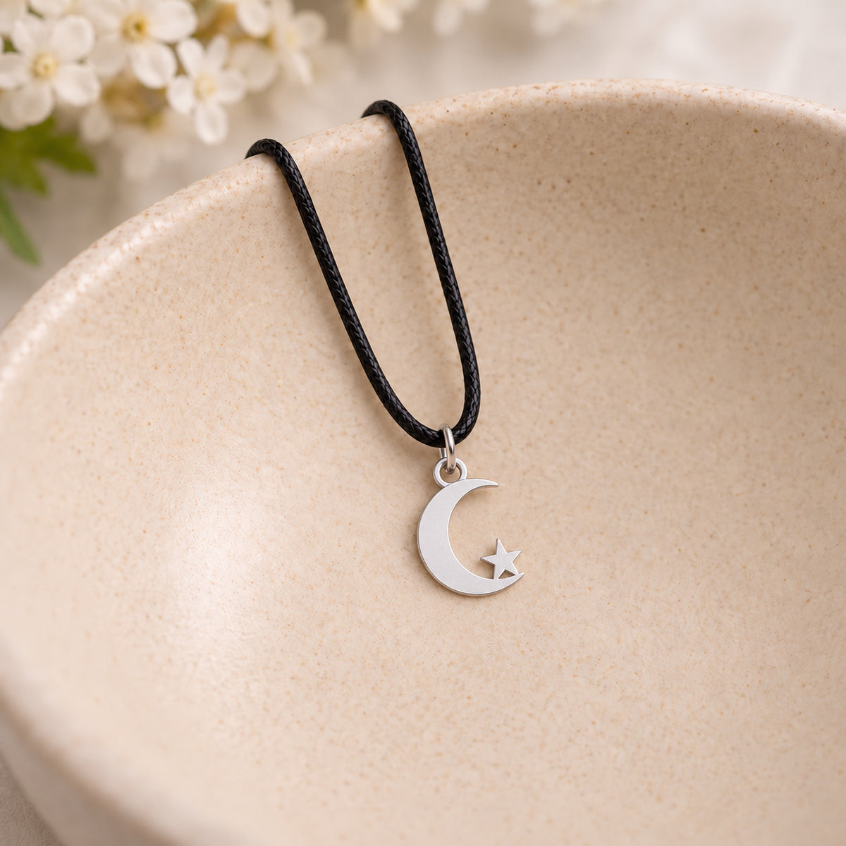 Silver crescent moon and star pendant on black cord in a speckled ceramic bowl
