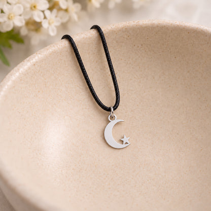 Silver crescent moon and star pendant on black cord in a speckled ceramic bowl