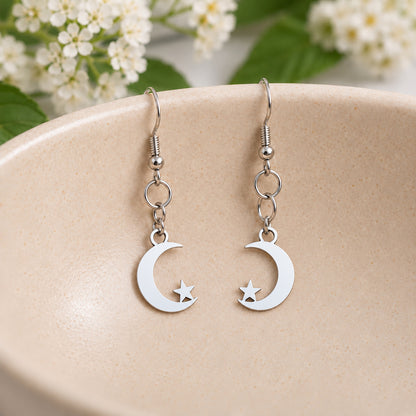 Mirrored silver-tone moon and star earrings resting in a speckled ceramic bowl