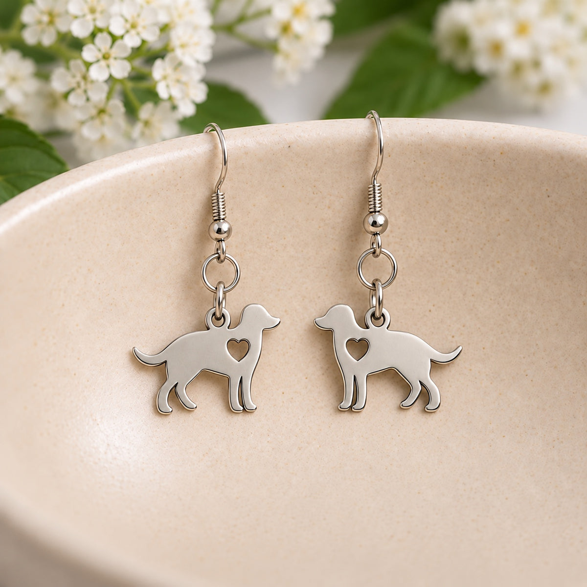 Silver dog earrings with heart cut-outs resting inside a speckled ceramic bowl