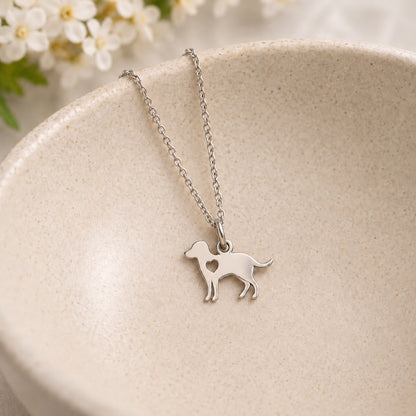 Silver dog pendant necklace with a heart cut-out resting in a speckled ceramic bowl