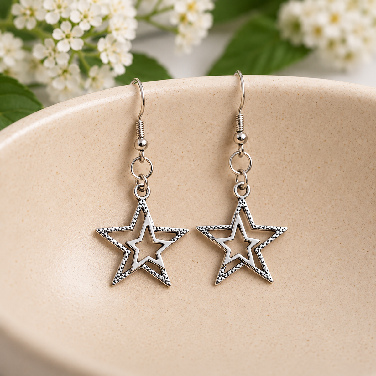 Silver double star earrings resting in a speckled ceramic bowl.