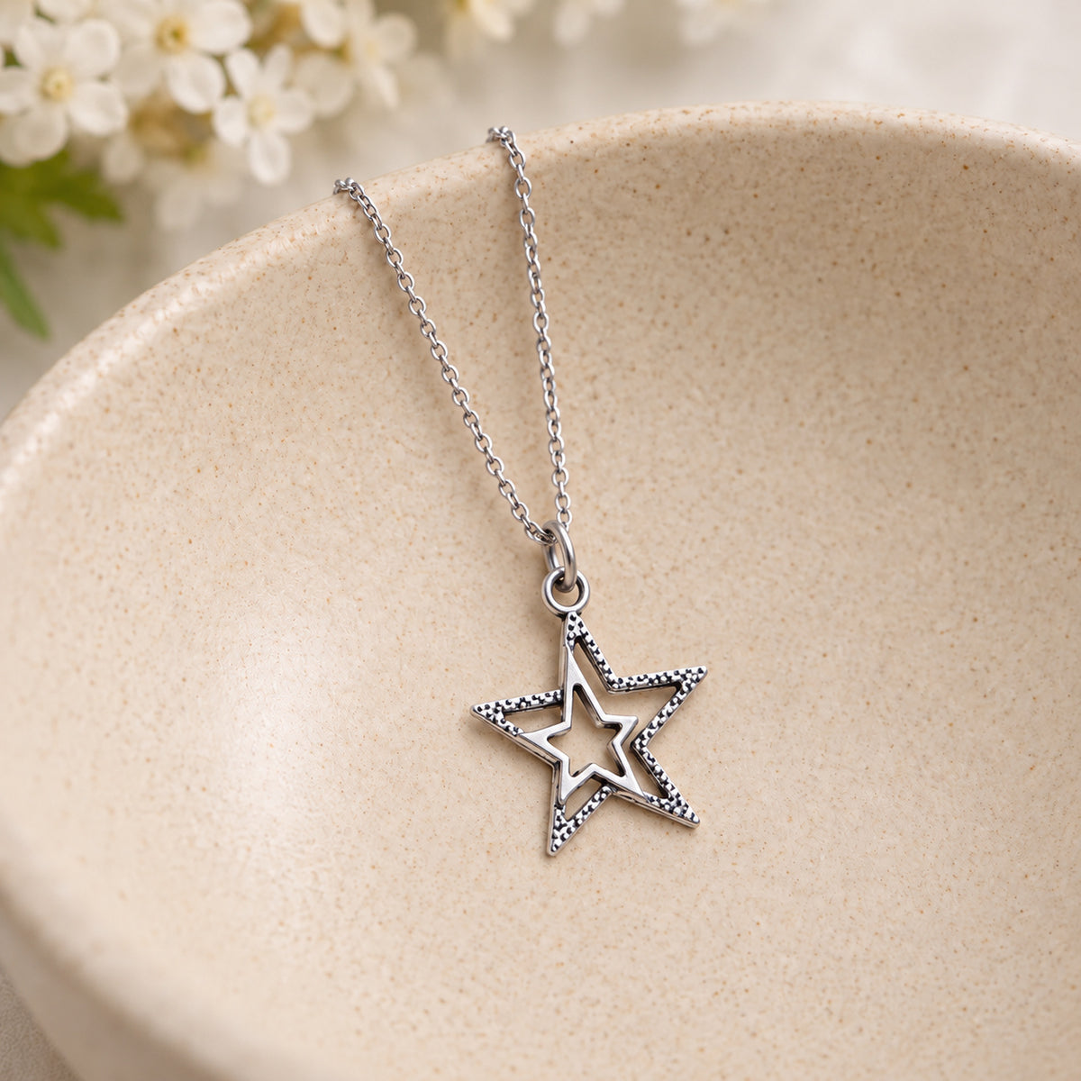 Silver double star necklace resting in a speckled ceramic bowl.