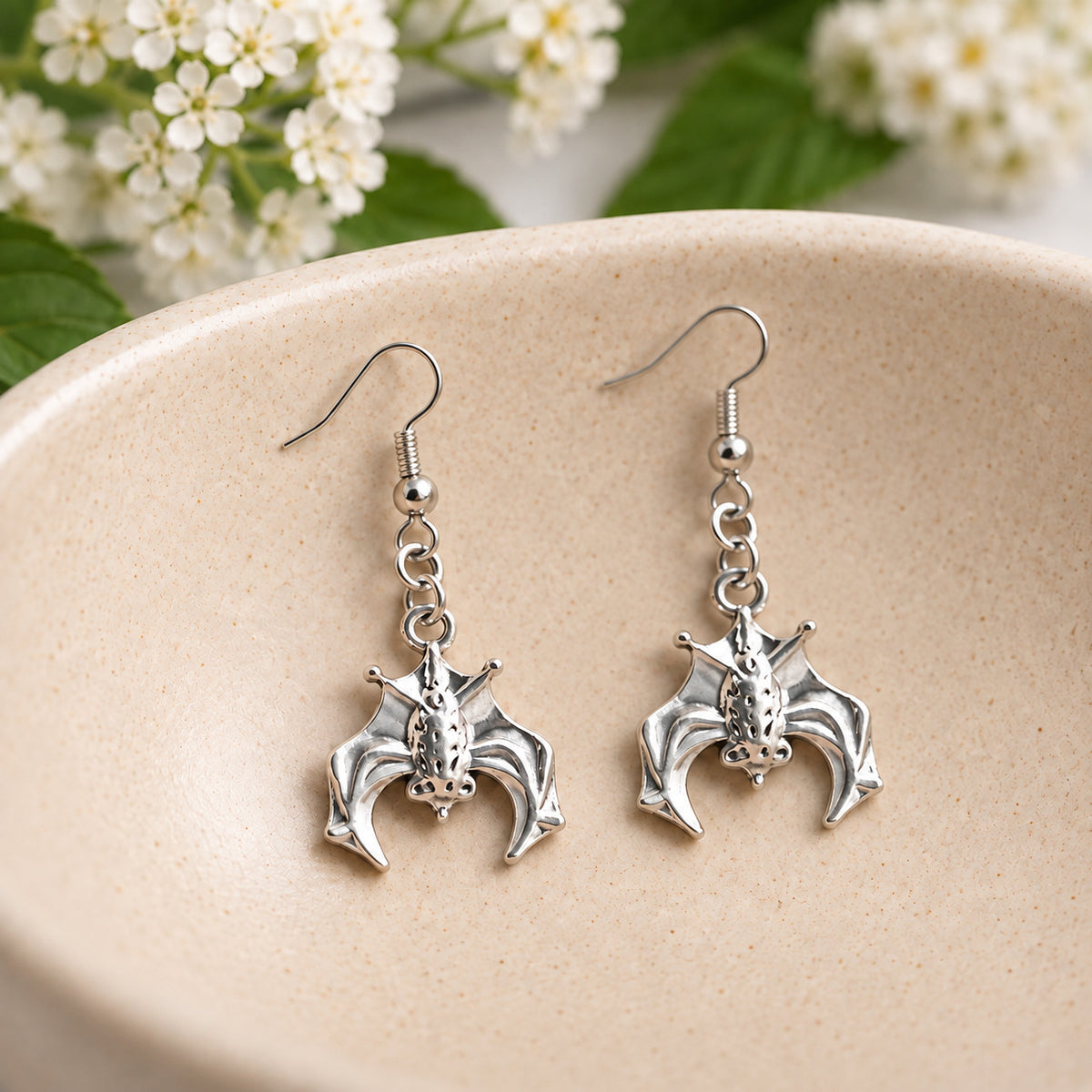 Silver hanging bat earrings in a speckled ceramic bowl