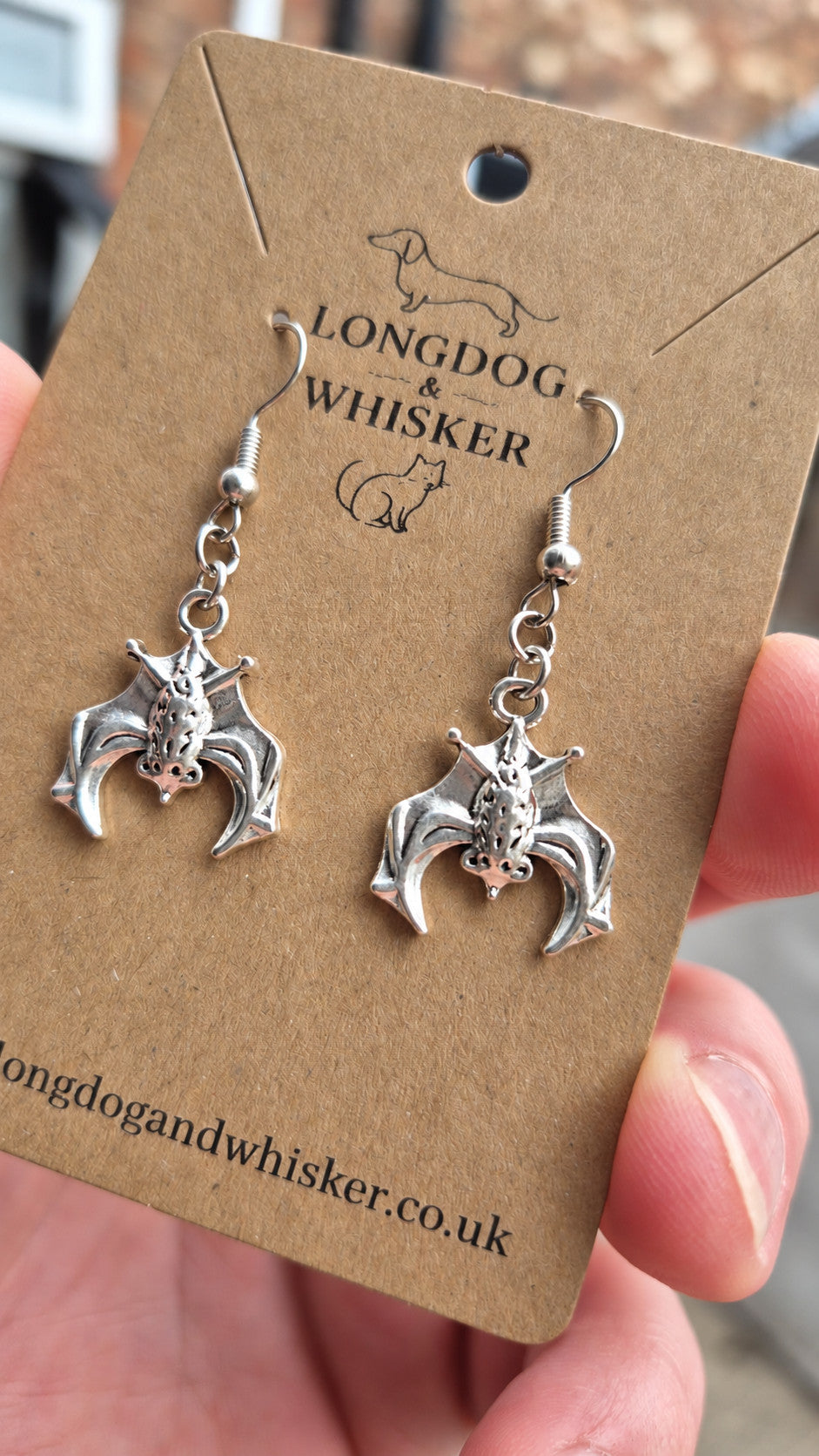Close-up of the all-silver hanging bat earrings and hooks on kraft card