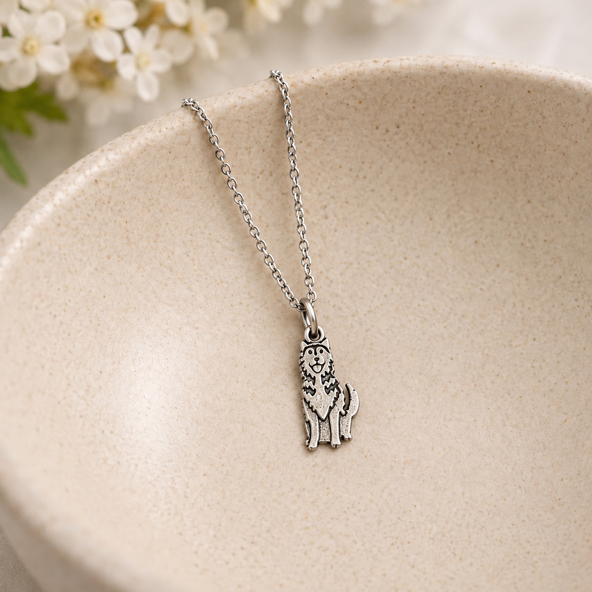 Silver-tone husky pendant necklace resting in a speckled ceramic bowl