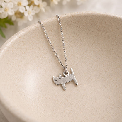 Silver-tone standing cat pendant necklace resting in a speckled ceramic bowl