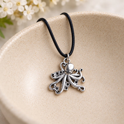 Silver-tone octopus pendant on black cord resting in a speckled ceramic bowl