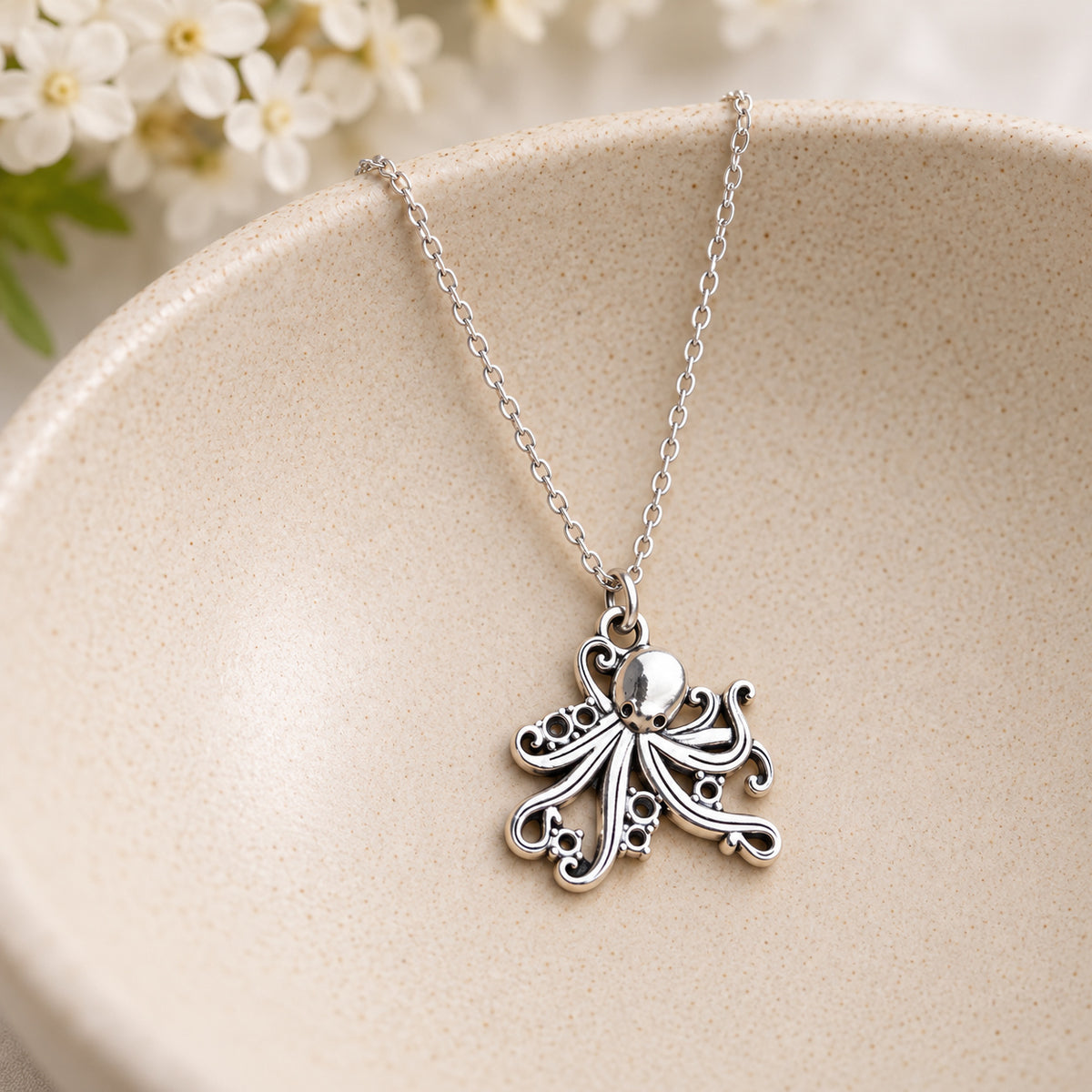 Silver-tone octopus chain necklace resting in a speckled ceramic bowl
