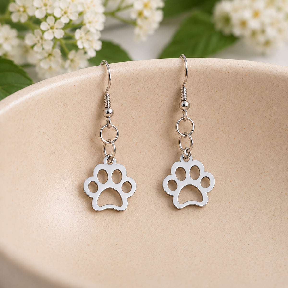 Silver paw print earrings resting in a speckled ceramic bowl
