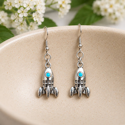 Silver-tone rocket earrings with turquoise details resting inside a speckled ceramic jewellery bowl