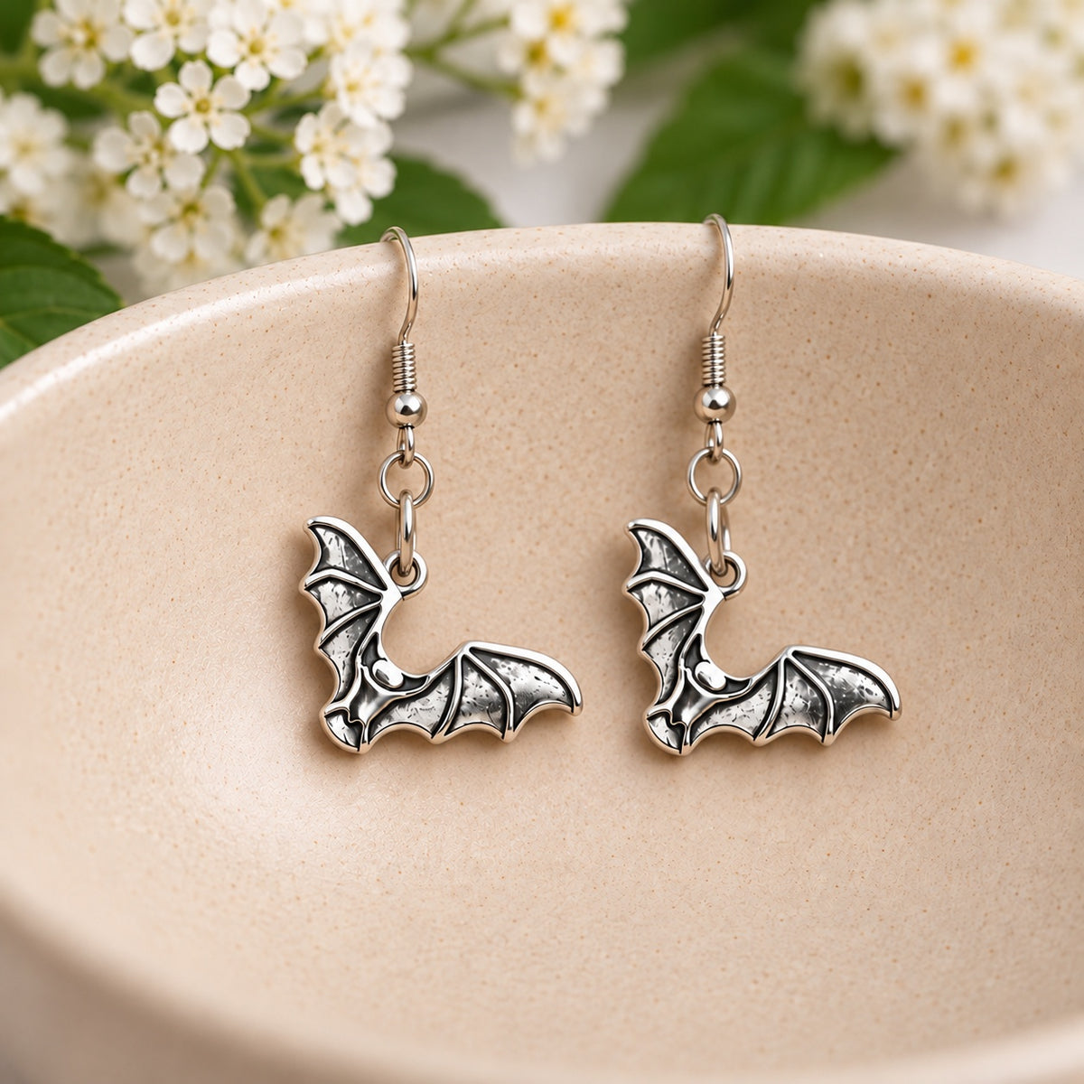 Pair of silver-tone bat earrings resting in a cream speckled ceramic bowl