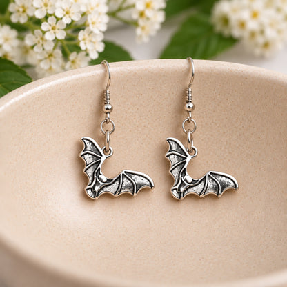 Pair of silver-tone bat earrings resting in a cream speckled ceramic bowl