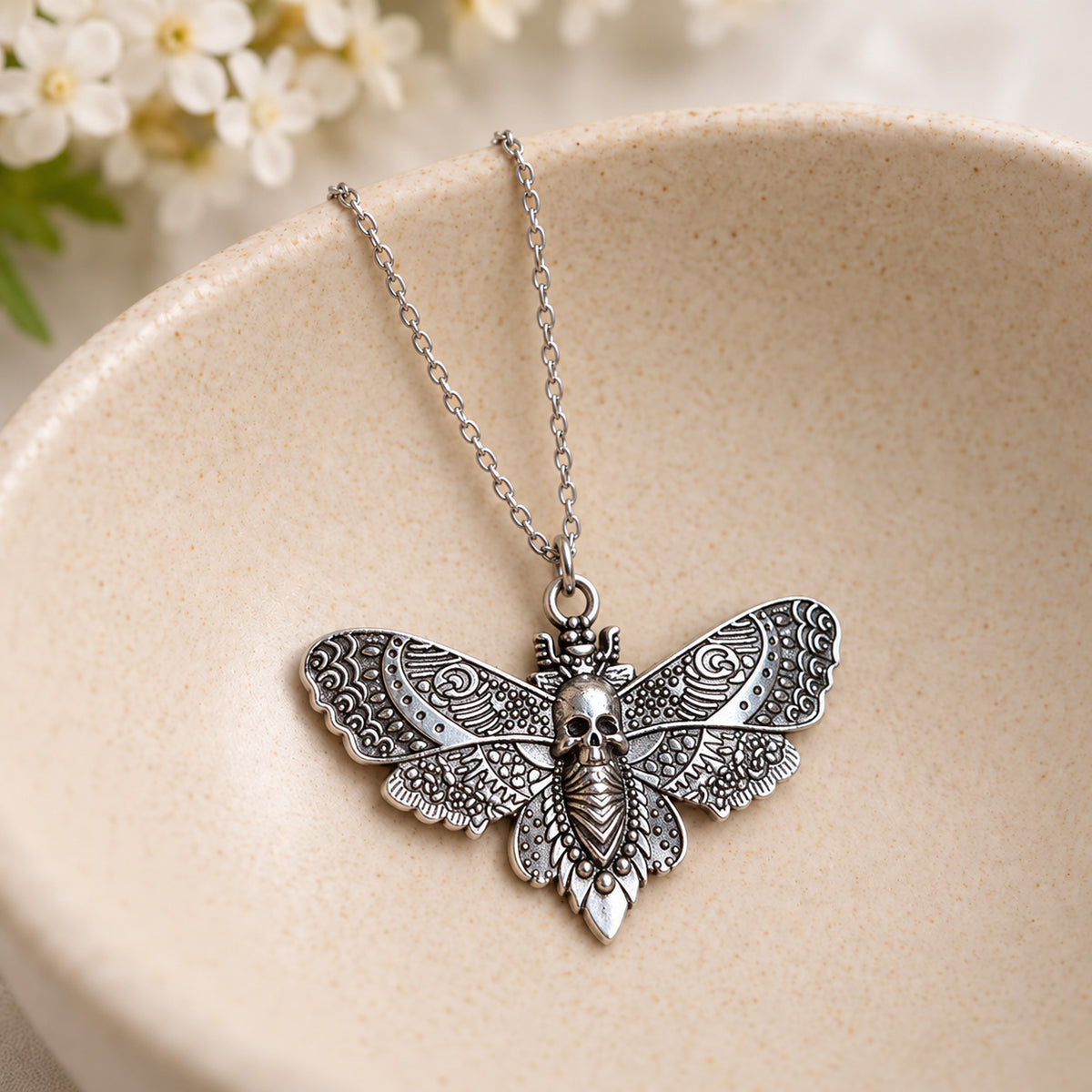 Silver skull moth pendant and silver chain resting in a speckled ceramic bowl